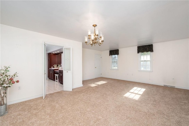 empty room with baseboards, a chandelier, and light carpet