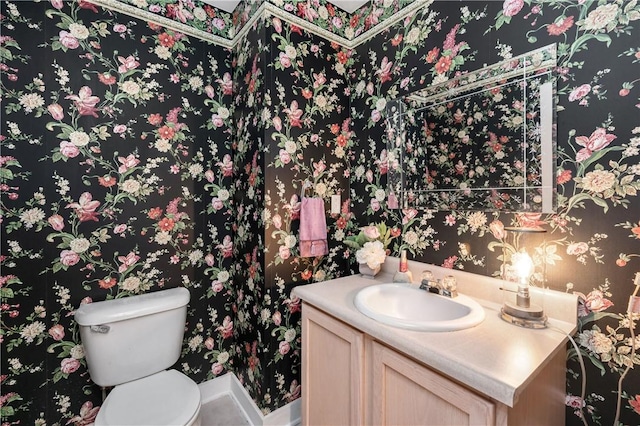 half bathroom featuring toilet, wallpapered walls, and vanity