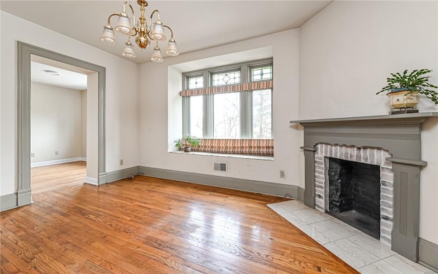 unfurnished living room with baseboards, visible vents, an inviting chandelier, hardwood / wood-style flooring, and a brick fireplace