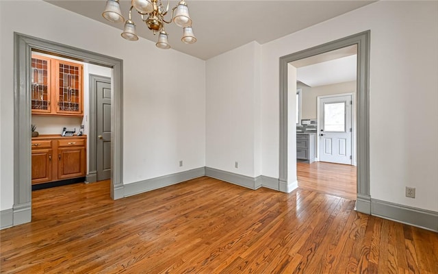 empty room with an inviting chandelier, baseboards, and light wood-type flooring