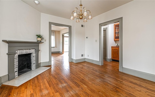 unfurnished living room with visible vents, baseboards, an inviting chandelier, hardwood / wood-style flooring, and a brick fireplace