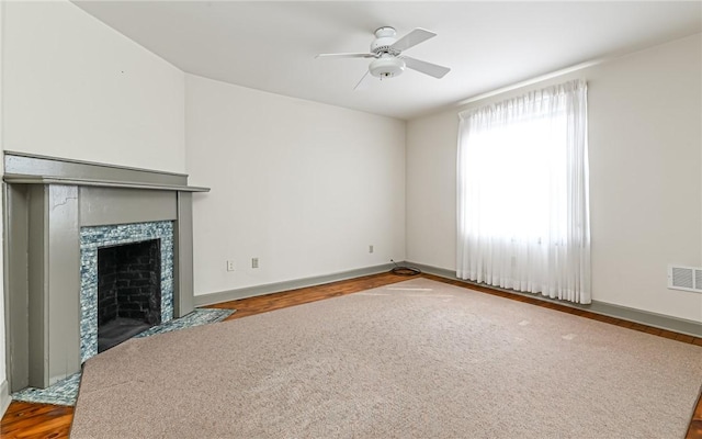 unfurnished living room with visible vents, wood finished floors, a ceiling fan, and a tile fireplace