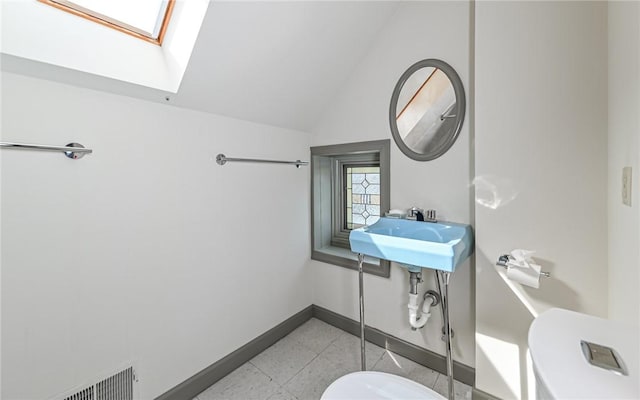 bathroom with visible vents, lofted ceiling with skylight, toilet, a sink, and baseboards