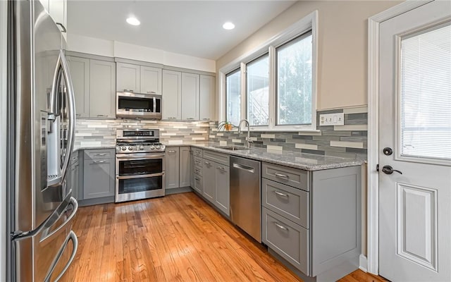 kitchen with backsplash, appliances with stainless steel finishes, gray cabinetry, and light stone countertops