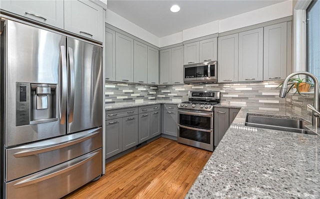 kitchen with a sink, gray cabinetry, backsplash, and stainless steel appliances