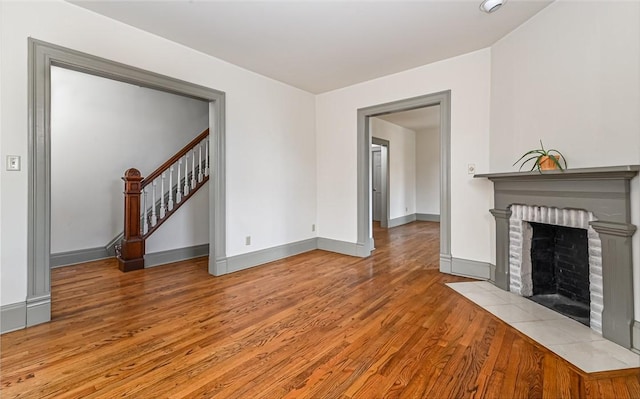 unfurnished living room with a fireplace, stairway, wood finished floors, and baseboards