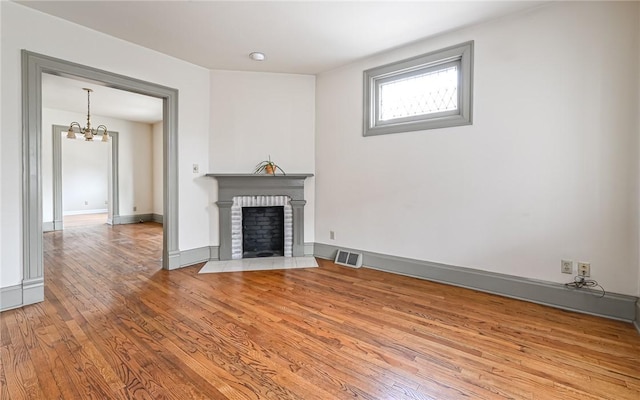 unfurnished living room featuring wood finished floors, visible vents, baseboards, a fireplace, and a notable chandelier