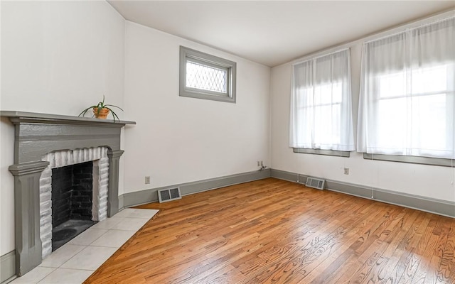 unfurnished living room featuring visible vents, baseboards, light wood-style floors, and a fireplace with flush hearth