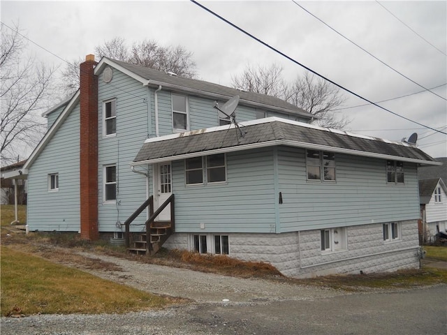 view of home's exterior with a shingled roof, a chimney, and entry steps