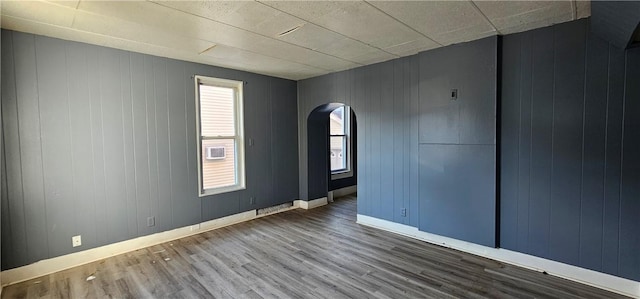 empty room featuring baseboards, arched walkways, and wood finished floors