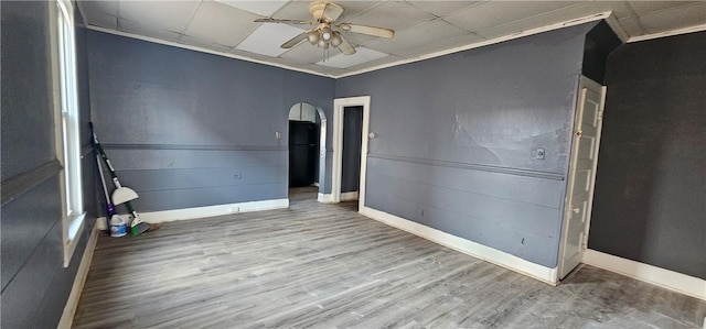 unfurnished room featuring a ceiling fan, wood finished floors, baseboards, arched walkways, and a paneled ceiling