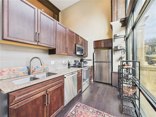 kitchen featuring a sink, appliances with stainless steel finishes, decorative backsplash, a towering ceiling, and dark wood-style flooring