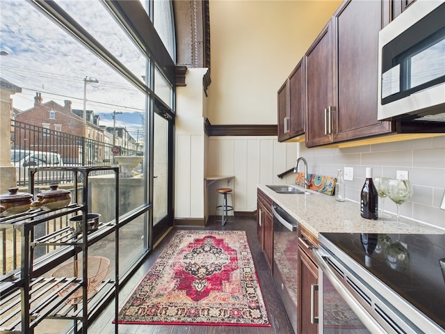 kitchen featuring light stone counters, a wainscoted wall, a sink, appliances with stainless steel finishes, and tasteful backsplash