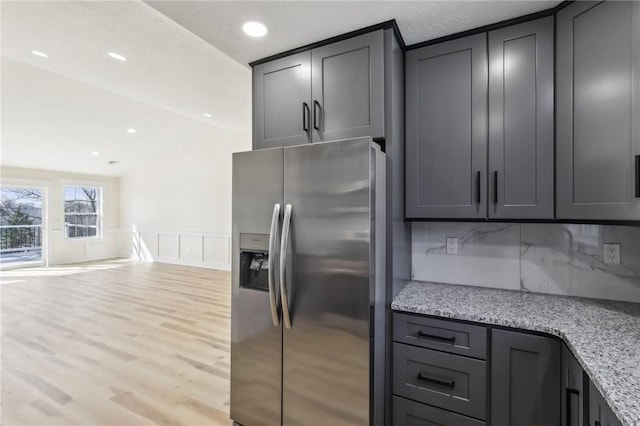 kitchen featuring light stone counters, light wood-style floors, gray cabinetry, and stainless steel fridge with ice dispenser