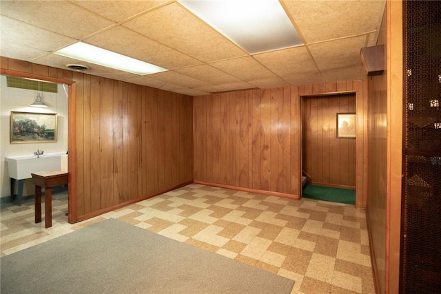 finished below grade area featuring a paneled ceiling, wooden walls, and baseboards
