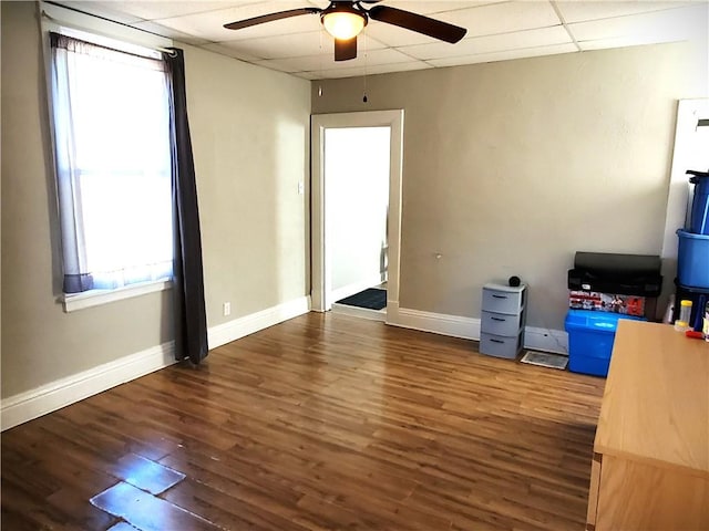 interior space with a drop ceiling, wood finished floors, baseboards, and ceiling fan