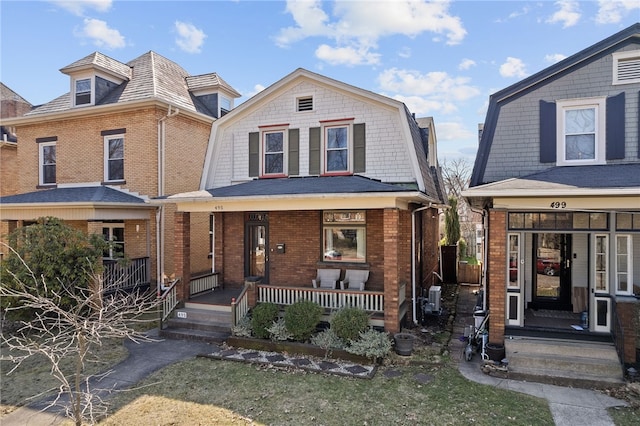 view of front of house with brick siding, a gambrel roof, and covered porch