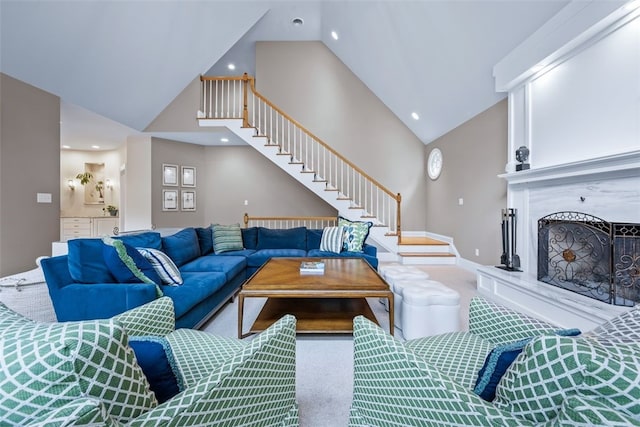 living area featuring carpet, baseboards, high vaulted ceiling, a high end fireplace, and stairs