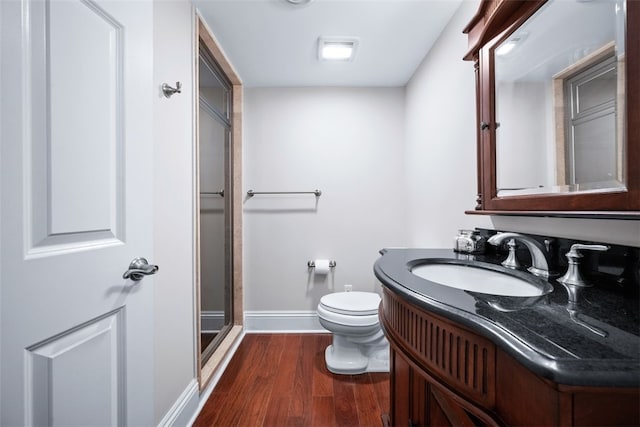 bathroom featuring a shower with door, baseboards, toilet, wood finished floors, and vanity