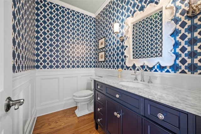bathroom with wainscoting, wallpapered walls, ornamental molding, and wood finished floors
