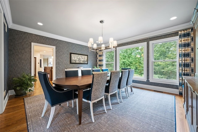 dining space featuring wood finished floors, baseboards, wallpapered walls, crown molding, and a chandelier