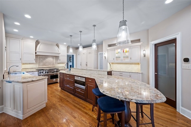 kitchen featuring wood finished floors, double oven range, custom exhaust hood, a sink, and white cabinets