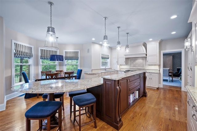 kitchen featuring a center island with sink, tasteful backsplash, custom exhaust hood, and wood finished floors