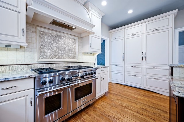 kitchen with custom exhaust hood, white cabinetry, light wood-type flooring, and range with two ovens