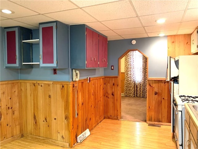 406 Peach St, City Of But Ne, PA 16001 - kitchen with white range with gas stovetop, wood walls, a drop ceiling, light wood-type flooring, and a wainscoted wall