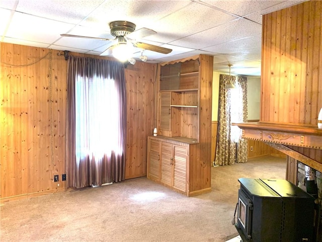 406 Peach St, City Of But Ne, PA 16001 - interior space with wooden walls, a wood stove, a ceiling fan, light colored carpet, and a paneled ceiling
