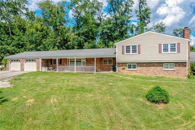 split level home featuring a front lawn, aphalt driveway, a porch, an attached garage, and a chimney