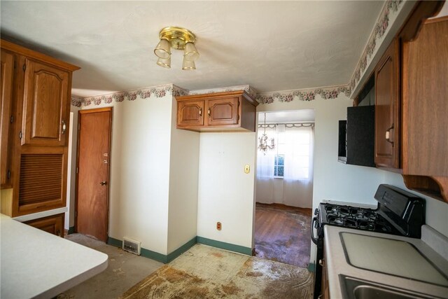 kitchen featuring visible vents, baseboards, range with gas stovetop, brown cabinetry, and a sink