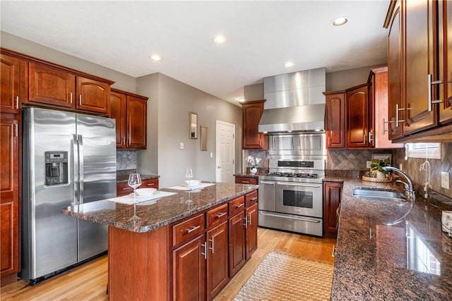 kitchen featuring a sink, stainless steel appliances, light wood-style floors, wall chimney range hood, and a center island