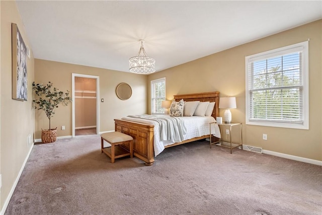 carpeted bedroom with a walk in closet, a notable chandelier, baseboards, and visible vents