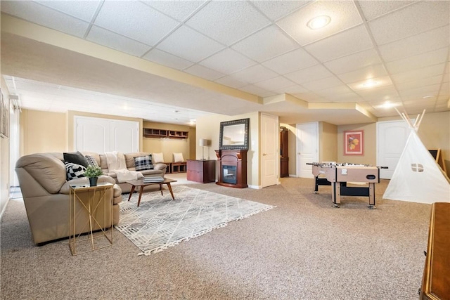 living room with a paneled ceiling, carpet floors, and a glass covered fireplace