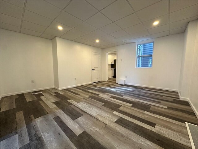 below grade area featuring baseboards, visible vents, a drop ceiling, and dark wood-type flooring