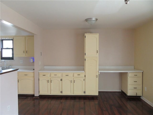 kitchen featuring baseboards, light countertops, dark wood-style floors, cream cabinetry, and a sink
