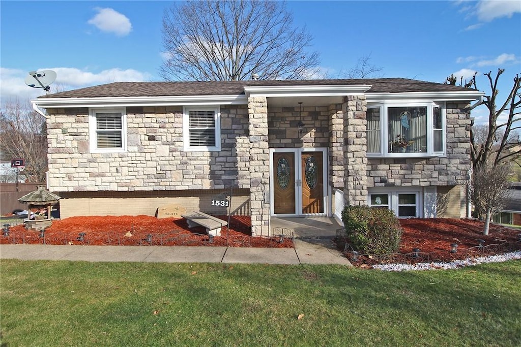 raised ranch featuring stone siding and a front yard
