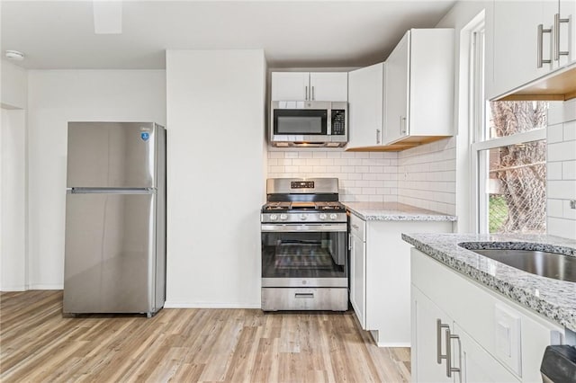 5021 Broad St, Garfield, PA 15224 - kitchen featuring stainless steel appliances, light stone counters, light wood finished floors, and tasteful backsplash