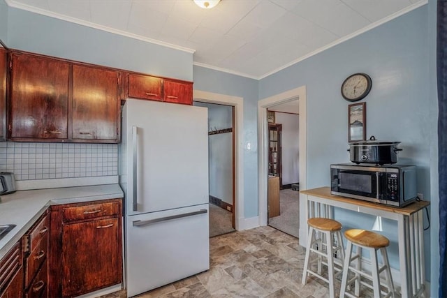 kitchen featuring freestanding refrigerator, stainless steel microwave, crown molding, backsplash, and light countertops
