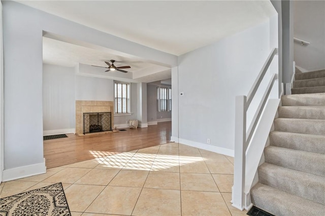 unfurnished living room with tile patterned flooring, stairs, a ceiling fan, baseboards, and a fireplace with flush hearth
