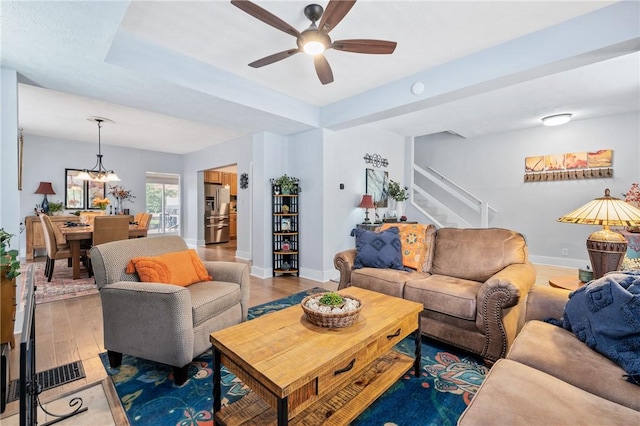 living area with ceiling fan, stairway, baseboards, wood finished floors, and a raised ceiling