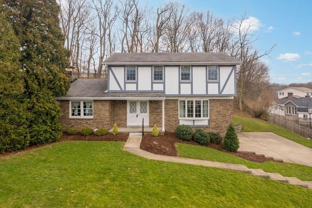 english style home featuring brick siding, fence, a front yard, stucco siding, and a chimney