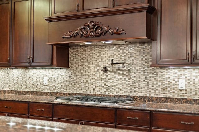 kitchen featuring dark stone countertops, tasteful backsplash, dark brown cabinets, and stainless steel gas stovetop