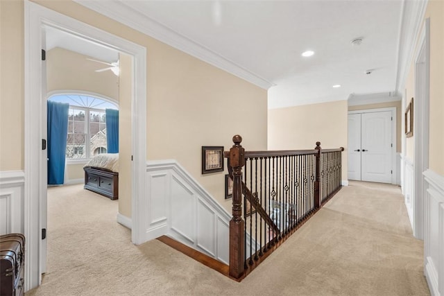 hallway with light carpet, wainscoting, crown molding, a decorative wall, and an upstairs landing