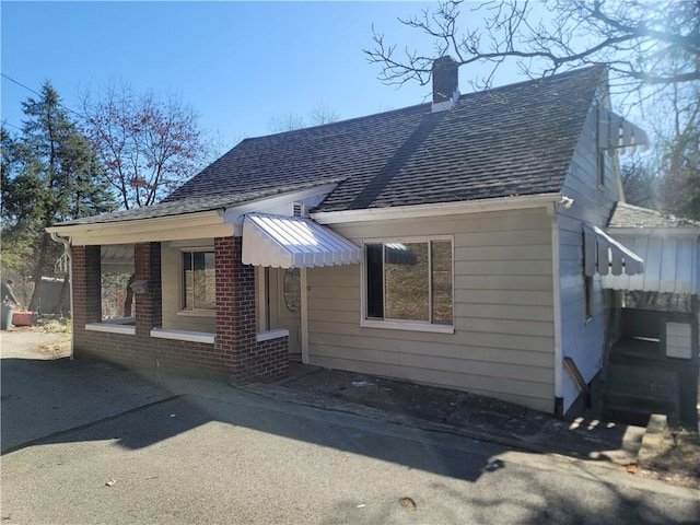 view of front facade with brick siding, a chimney, and a shingled roof