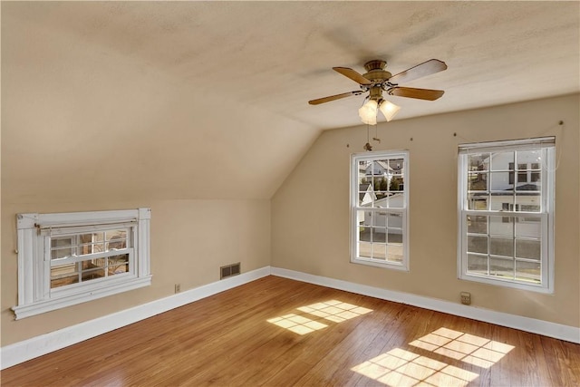 additional living space featuring visible vents, hardwood / wood-style flooring, baseboards, ceiling fan, and vaulted ceiling