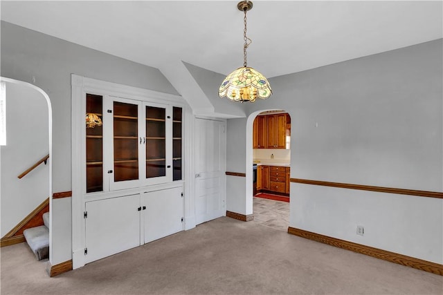 unfurnished dining area featuring baseboards, arched walkways, light colored carpet, and stairs