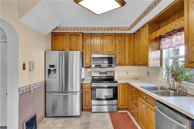kitchen featuring visible vents, brown cabinets, a sink, stainless steel appliances, and arched walkways