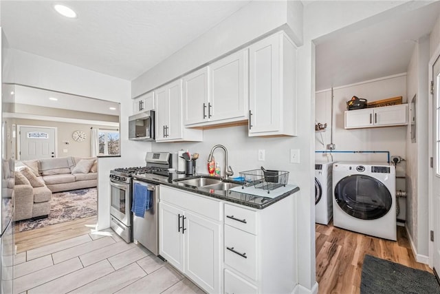 kitchen featuring washing machine and clothes dryer, a sink, white cabinets, appliances with stainless steel finishes, and light wood-type flooring